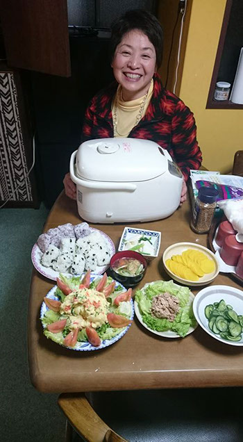 手作りのおにぎりやサラダなどを前に、満面の笑みの山田みやこ